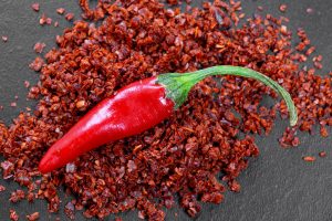 Red fresh chili pepper and dry ground hot pepper on black background