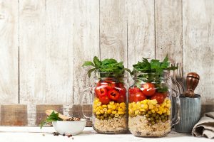 Homemade healthy layer salad in mason jars on a wooden backgroun