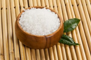 Two green leaves and sea salt in wooden bowl